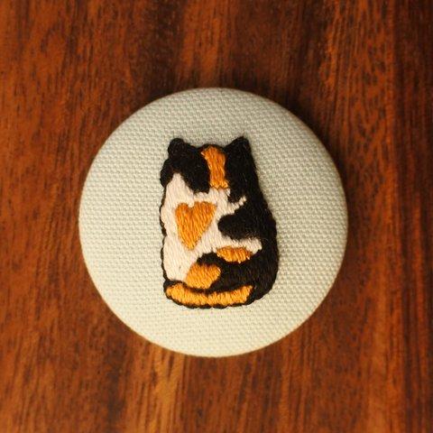 「ちょこんと座る三毛猫のみーちゃん」の刺繍くるみボタンマグネット（刺繍布の色：サックスブルー）